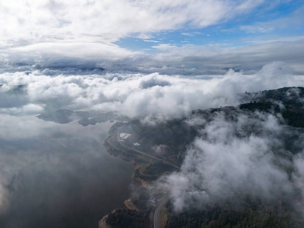 This aerial photograph captures a dramatic landscape where dense clouds hover above rugged mountains. The visual style is naturalistic, emphasizing the vastness and tranquility of the scene. It's ideal for nature-themed projects or environmental studies.