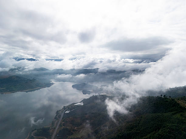 This aerial photograph captures a dramatic landscape where dense clouds hover above rugged mountains. The visual style is naturalistic, emphasizing the vastness and tranquility of the scene. It's ideal for nature-themed projects or environmental studies.