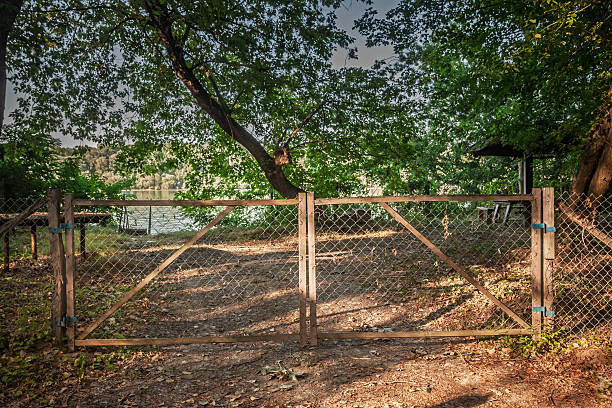 istock Double wooden frame gate with chain link panels blocks a dirt path under leafy trees, marking private riverbank access in quiet woodland. Warm afternoon light, deep shade create a rustic secluded mood 2230883283