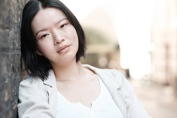 istock Young asian woman leaning against a wall with a serious expression 2230888239