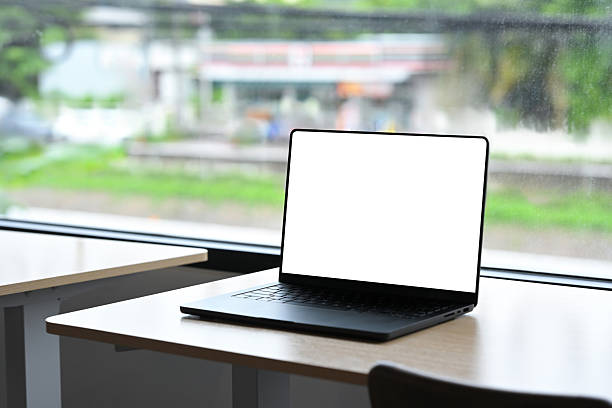 istock Modern black laptop computer with empty white screen placed on wooden desk near large window. 2230896578