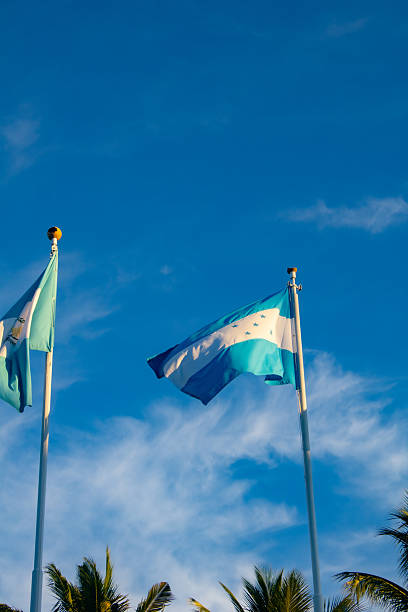 Honduras and Guatemala National Flags waving on flag poles on a cloudy blue day