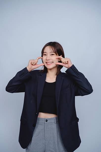istock Smiling young woman in oversized suit jacket shows cheerful expression against plain background while posing playfully and engaging with the camera 2230902631