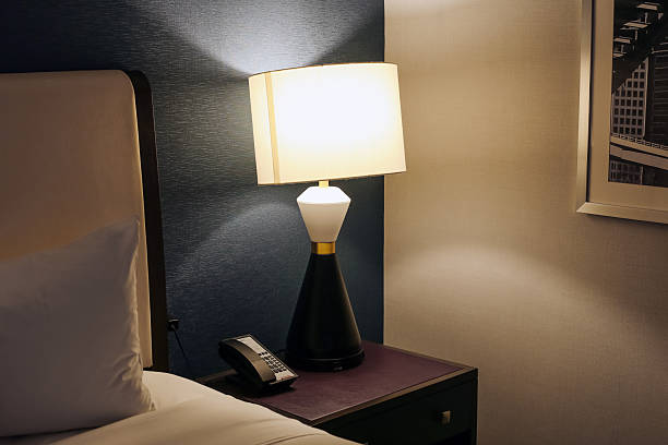 istock Cozy hotel room interior with bedside lamp. Warm light creating relaxing atmosphere. Bed with white pillow and nightstand with phone. 2230902903