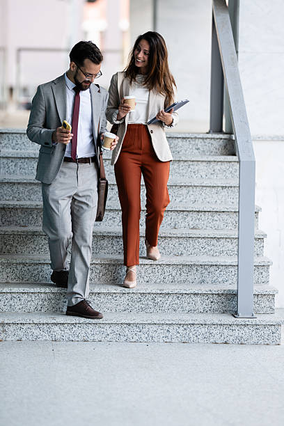 istock Business colleagues walking down stairs while having coffee and using smartphone 2230907961