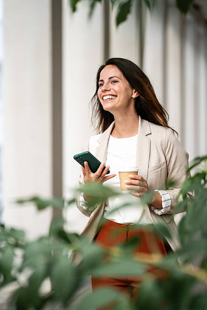 istock Smiling businesswoman walking with smartphone and coffee in modern office 2230908024