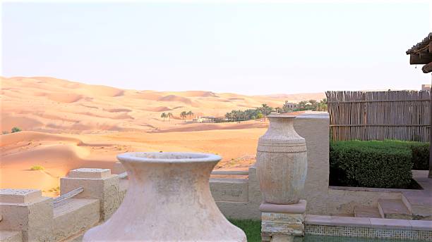 istock Desert landscape framing rolling sand dunes between elegant ceramic vases, palm trees silhouetted near distant architectural structure in United Arab Emirates, highlighting serene luxury 2230908597