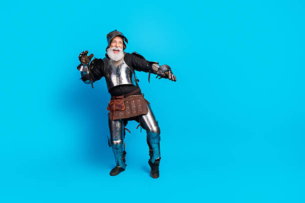 istock Elderly man in medieval knight armor posing with a cheerful expression against a vibrant blue backdrop, evoking history 2230915285
