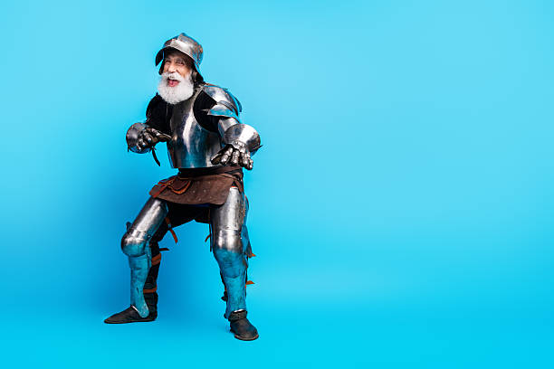 istock Elderly man in shiny medieval knight armor posing on light blue background 2230915290