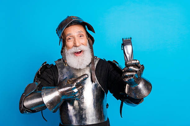 istock Elderly man in medieval knight armor holding a grooming tool on a vibrant blue background, showcasing humor and history. 2230915319