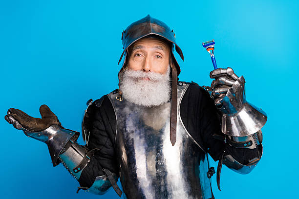 istock Bearded man dressed as a medieval knight holding a razor with a humorous expression against a blue background 2230915322
