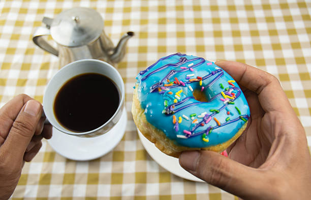 Stock image of a cup of piping hot black coffee served on a table alongside a plate of donuts. The composition highlights the perfect pairing of coffee and sweet snacks, creating a warm and inviting atmosphere. Ideal for illustrating breakfast moments, coffee breaks, or lifestyle concepts related to relaxation, comfort, and enjoying simple pleasures.