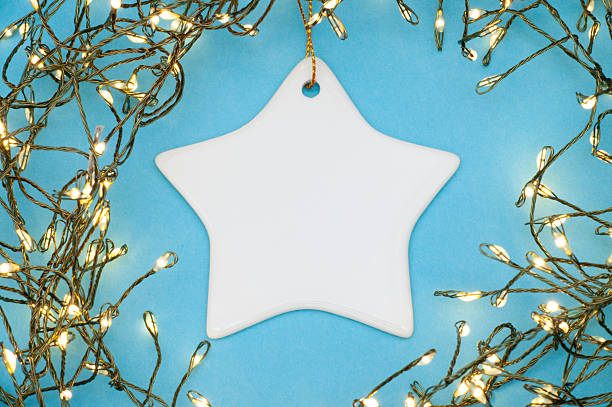 Flat lay of a star-shaped ceramic ornament surrounded by Christmas string lights on blue background. Perfect festive decoration for cards, winter holidays, New Year, and cozy seasonal designs.