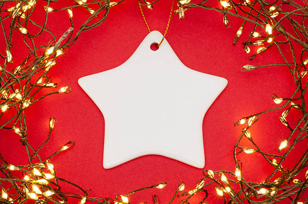 Flat lay of a star-shaped ceramic ornament surrounded by Christmas string lights on red background. Perfect festive decoration for cards, winter holidays, New Year, and cozy seasonal designs.