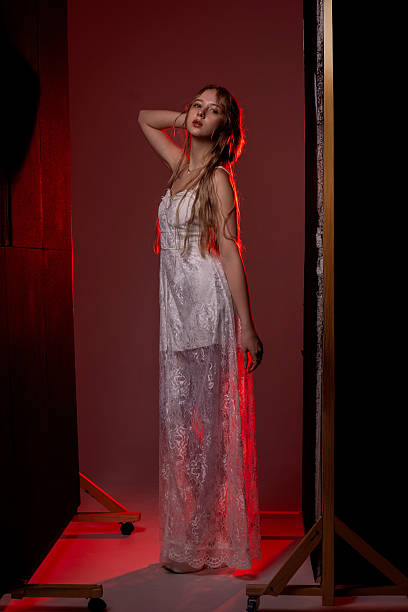Model showcases a white lace dress in a studio with creative lighting, striking a pose that emphasizes elegance and artistry.
