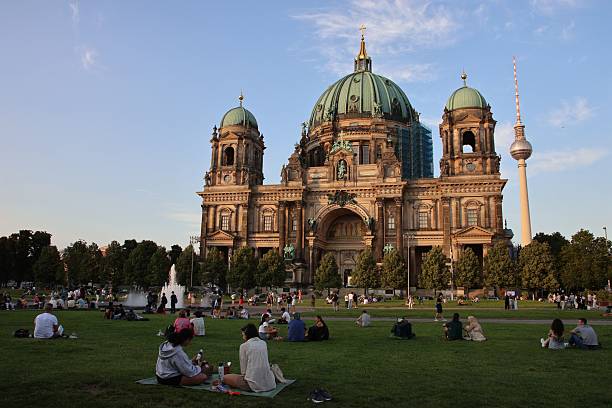 Berlin, Germany – August 12, 2025: Berlin Cathedral illuminated by sunlight with people relaxing in the park