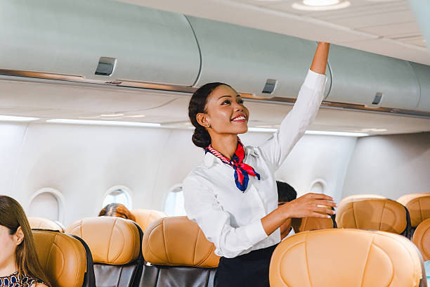istock Smiling flight attendant closing an overhead bin inside a modern airplane cabin with passengers seated. 2230925205