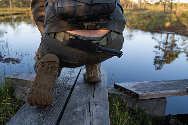 istock Adventurous hiker with a survival knife and backpack exploring a remote swamp on a wooden path at sunset. 2230927265