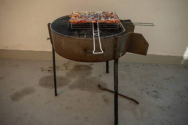 Small round barbecue grilling meat on a terrace, surrounded by dirty floors and white walls, creating a casual outdoor cooking scene perfect for summer meals and gatherings