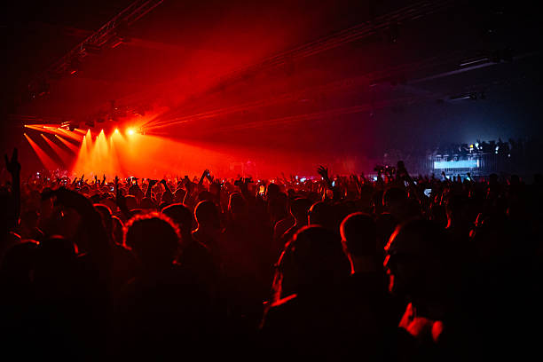Fans raising hands and enjoying live performance of a music band, illuminated by red stage lights