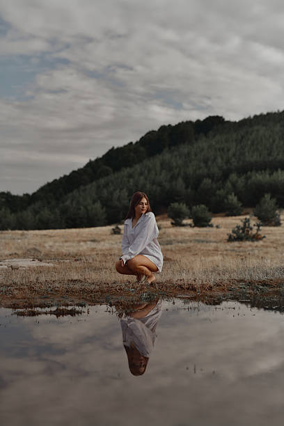 Peaceful Female Experiencing Nature While Kneeling Beside Water Reflection