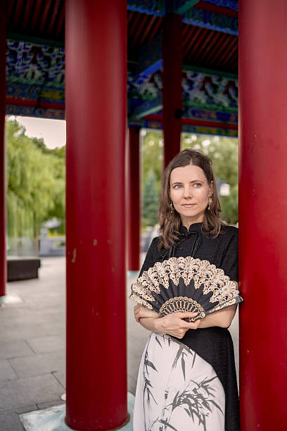 istock Elegant woman holding decorative fan by red columns 2230952105