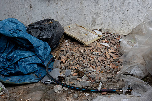 Piles of white doors, wooden frames, and garbage bags are stacked outside a building, illustrating urban waste and construction debris in a city setting during the day.