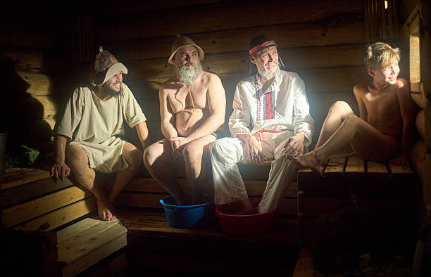 Two men and family (father and son) are sitting on a wooden bench at Russian steam bath (banya). They are steaming, relaxing and talking each other