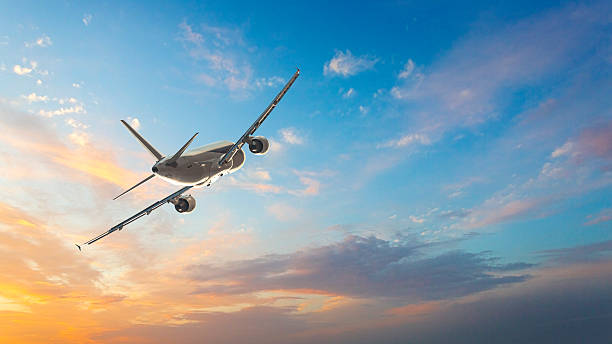 White passenger airplane flying in sunset sky with orange clouds