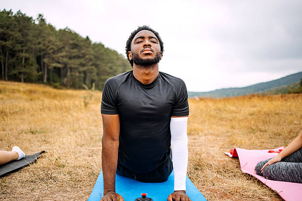 Young adult man relaxing in nature practicing yoga on exercise mats