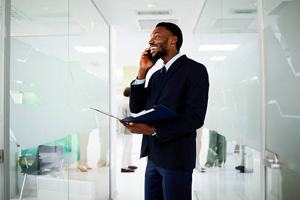 istock Businessman smiling while talking on the phone and holding documents in modern office corridor 2230971492