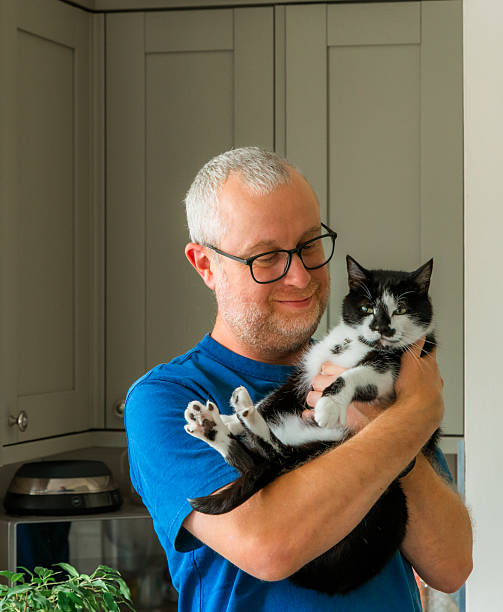 Close up portrait of a mid adult male pet owner cuddling with his black and white pet cat in his kitchen at home.