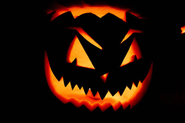 A Halloween pumpkin lit up at night. The pumpkin is hand-carved and reflects red light thanks to the candle inside. Fear concept