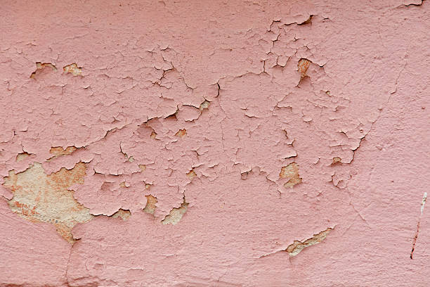 A wall with a pink paint that has some cracks and peeling. The wall is made of concrete