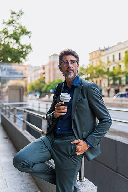 istock Elegant businessman drinking coffee on city sidewalk 2230979273