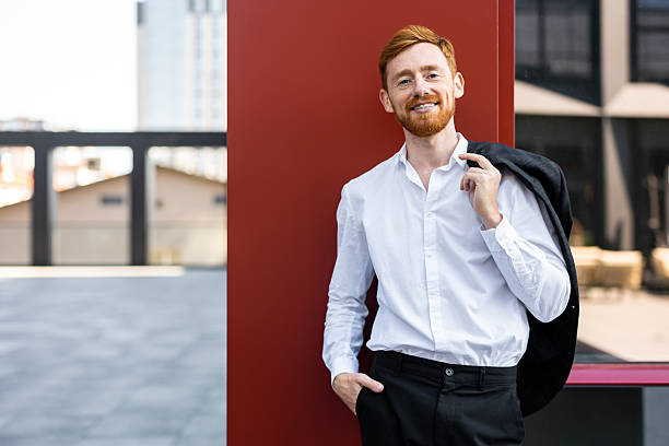 istock Ginger bearded man in white shirt posing outside by red building wall 2230979987