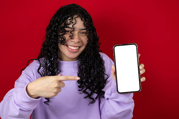 istock Cheerful young woman pointing at her cell phone with blank screen for copyspace 2230989684