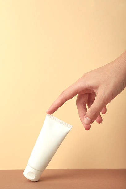 istock Hand holding blank white plastic tube on beige background. Vertical photo 2230998427
