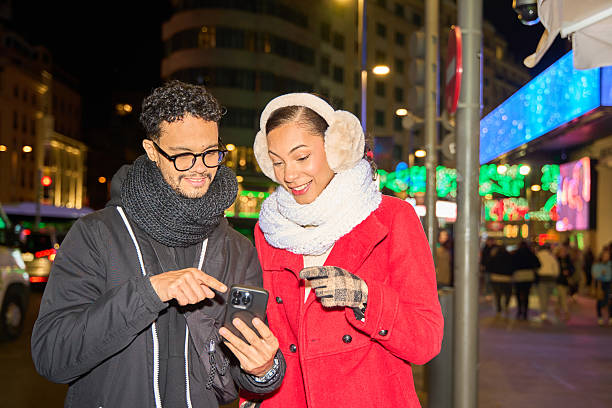 istock Young couple using smartphone in christmas decorated city at night 2231006734