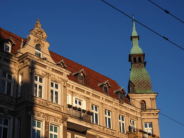 An ornate historic tenement house with decorative facade and a green-roofed tower in Szczecin, Poland, captured in warm evening light against a clear blue sky.