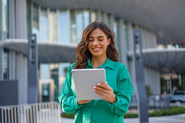 istock Young businesswoman smiling while using a digital tablet in a vibrant, modern cityscape, showcasing her connection and professionalism 2231018058
