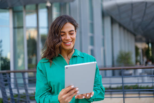 istock Professional woman working on digital tablet, standing confidently near modern office skyscraper with urban skyline background 2231018795