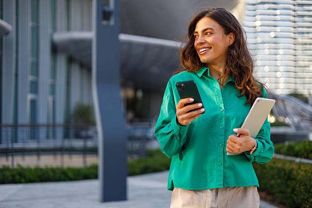 istock Professional female professional working remotely, checking digital devices with confident smile near city skyline background 2231020227
