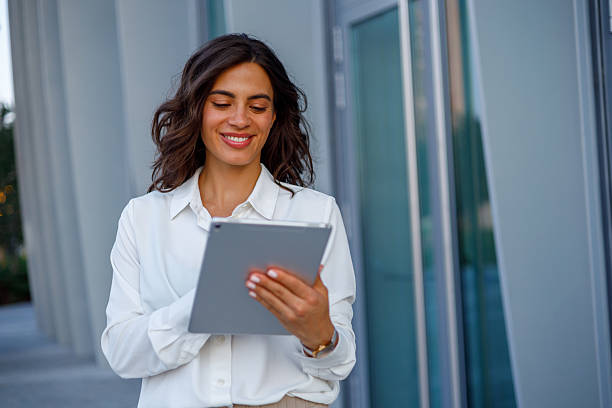 istock Young businesswoman smiling and using digital tablet while walking outside modern office building 2231020228