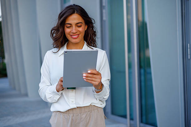 istock Smiling young businesswoman walking outdoors while engaging with a digital tablet, enjoying the vibrant city atmosphere and modern technology 2231020286