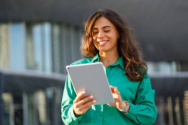 istock Young businesswoman using a digital tablet and smiling while standing in front of a modern office building 2231020514