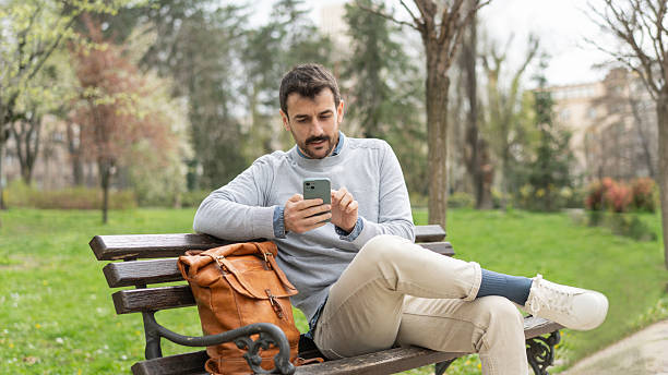 istock Man Relaxing on a Bench While Using His Smartphone Outdoors 2231023474