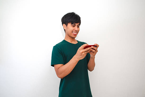 istock Happy excited young Asian man playing mobile game with smartphone, isolated on white background 2231030229