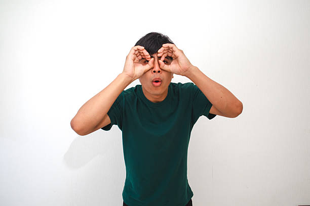 istock Portrait of a curious young Asian man looking through hand binoculars gesture with a surprised expression, isolated on a white background, perfect for creative advertising 2231031313