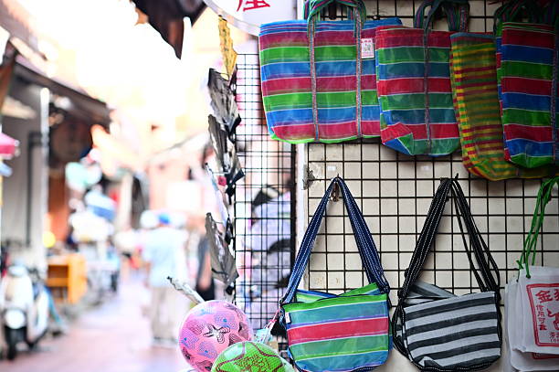 Taiwan - Aug 12, 2025: Vibrant striped and patterned Taiwanese gaji bags hang on a wire display rack at a bustling night market stall, with decorative balls and a blurred crowd in the background.